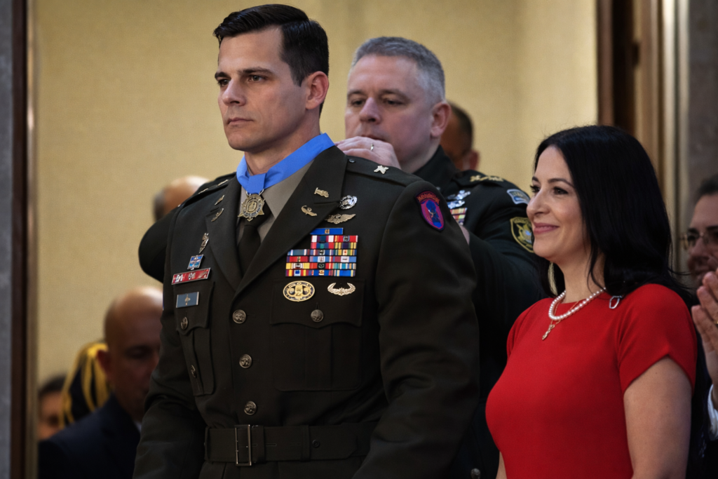 Chief Warrant Officer Eric Slover receiving the Medal of Honor during a formal ceremony while standing in Army dress uniform beside his wife.